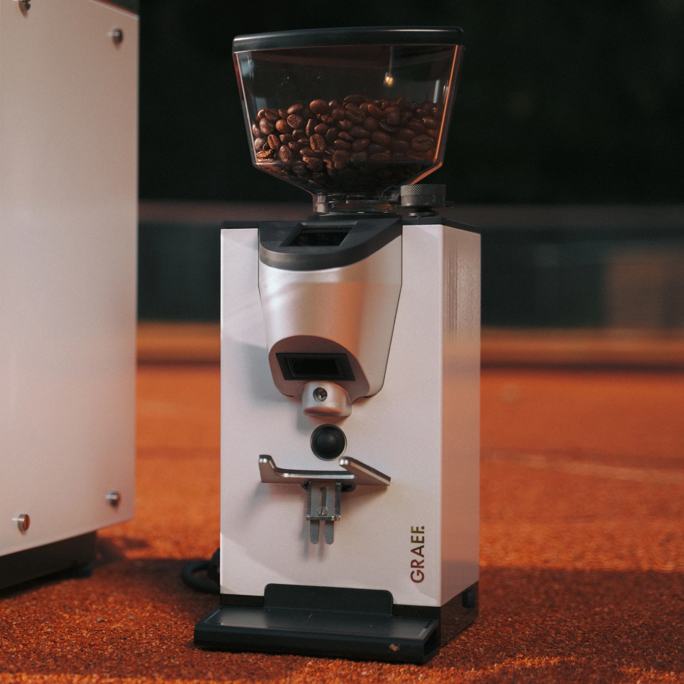 Graef coffee grinder on orange surface with coffee beans in the hopper.