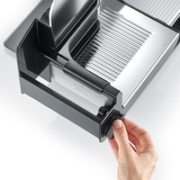 Primo piano di un'affettatrice nera con una mano che gira una manopola su una superficie bianca