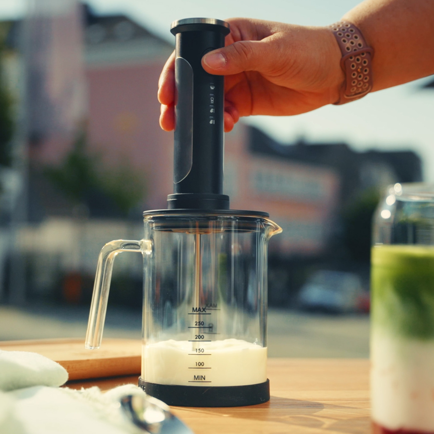 Une main tient un mousseur à lait au-dessus d'un verre de lait.