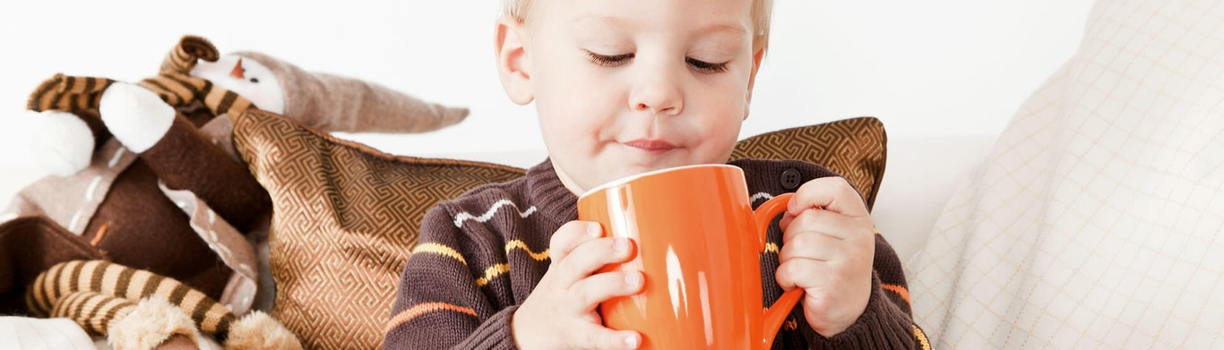 Jeune enfant buvant dans une grande tasse orange, confortablement installé sur un canapé.