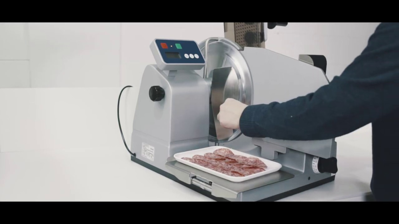 Affettatrice taglia salame. Persona usa la macchina. Fette su vassoio. Macchina argento.