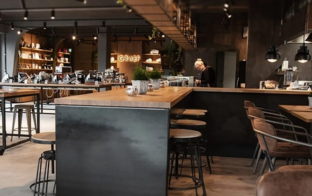 A cafe with bar stools, tables, and a person working behind the counter.