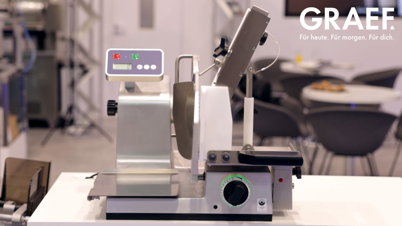 Affettatrice su un tavolo, logo GRAEF sullo sfondo, design moderno.