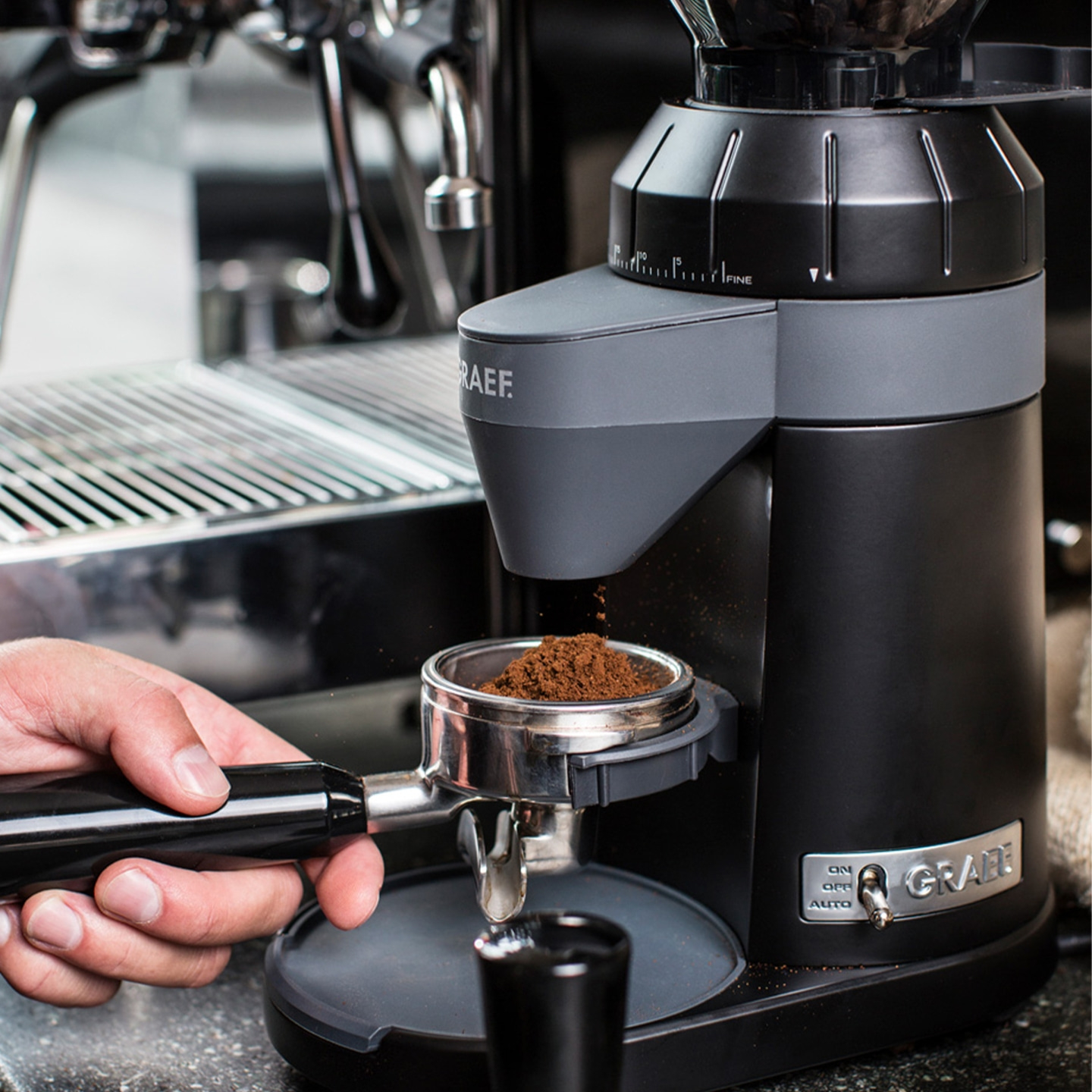 Coffee grinder grinding coffee powder into a portafilter, close-up, black.