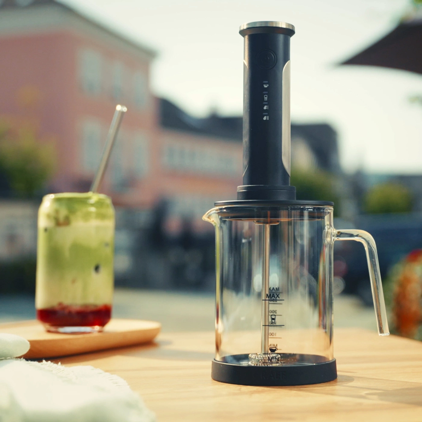 Macchina da caffè con caraffa in vetro e una bevanda verde accanto.