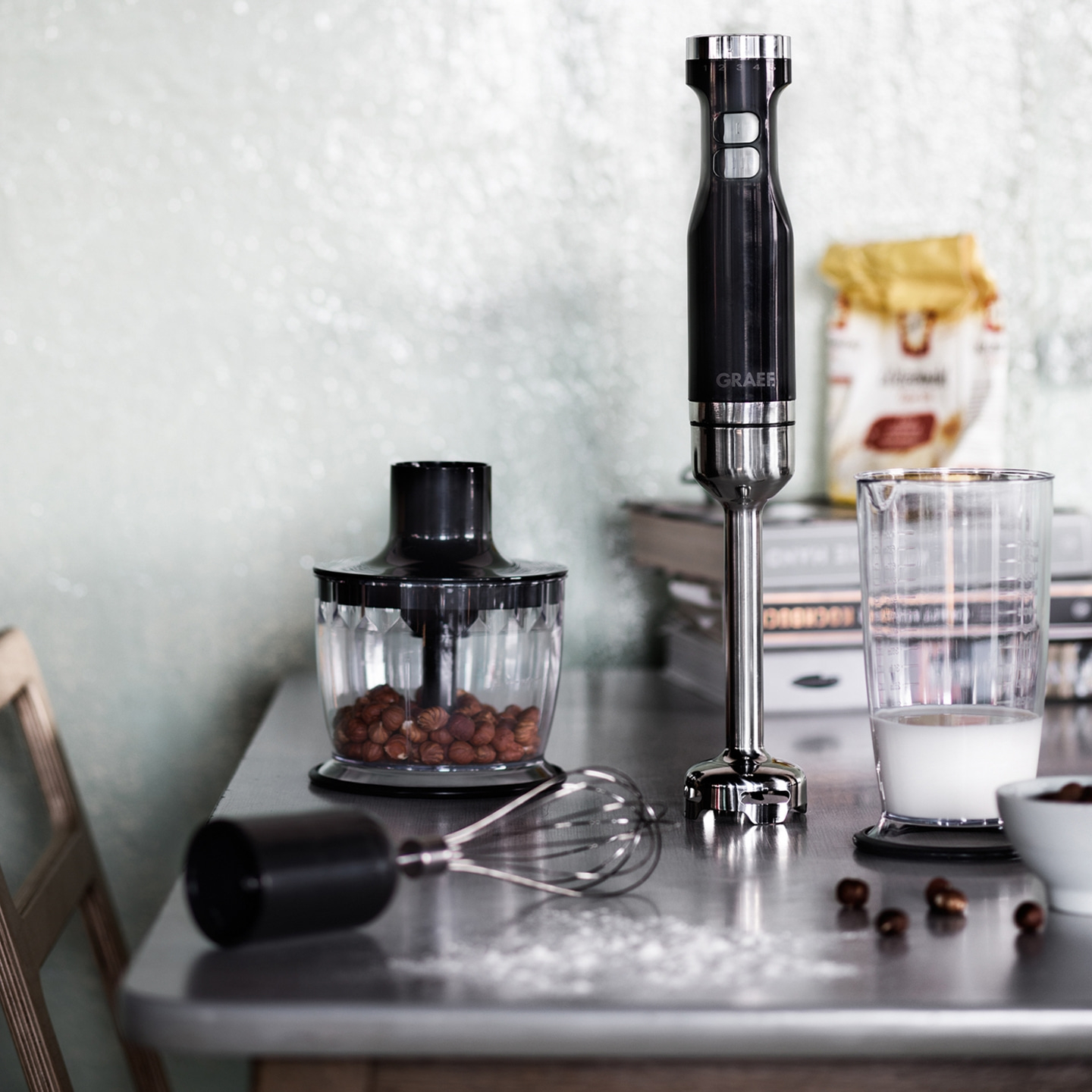 Ustensiles de cuisine sur une table : mixeur, récipient, lait, noix, fouet et ingrédients.