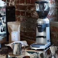 Moulin à café avec grains, accessoires et logo GRAEF sur la table.