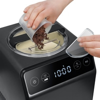 Person pouring chocolate pieces into an ice cream maker. Black device with display.