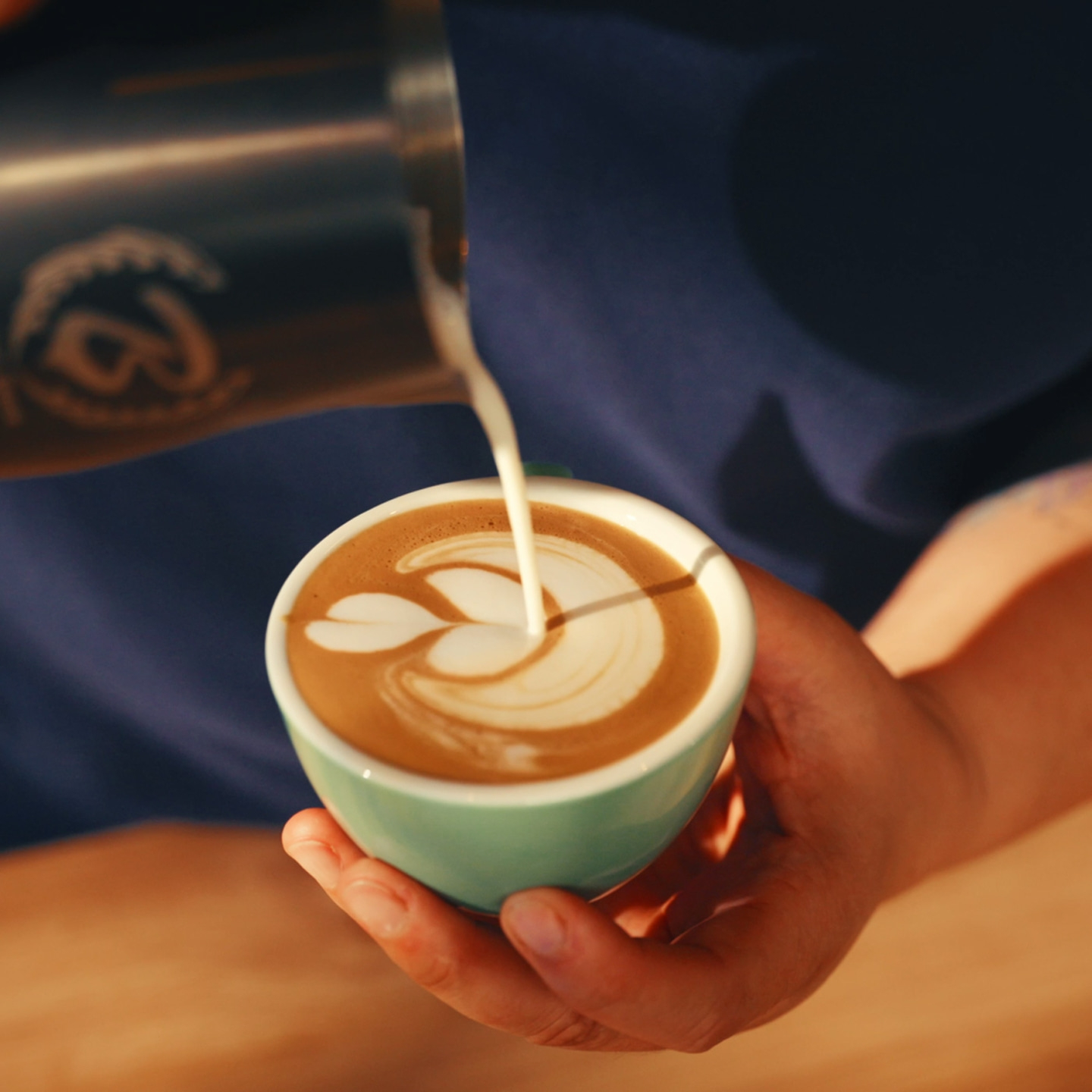 Barista pouring latte art into a coffee cup.