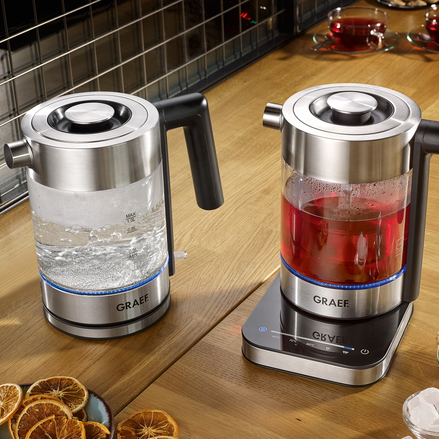 Two electric kettles on a wooden table with tea and decorations, GRAEF brand.