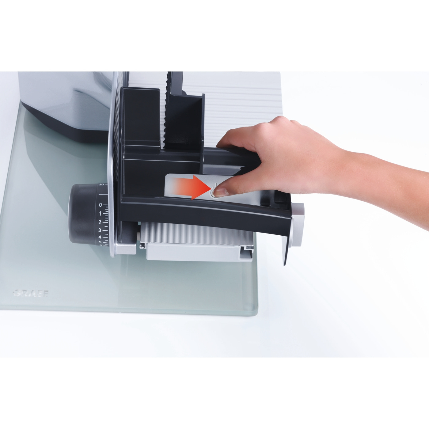 Primo piano di un'affettatrice con una mano che preme un pulsante per azionarla, con una freccia.