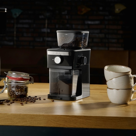 Coffee grinder with beans, cups, and coffee beans on wooden surface