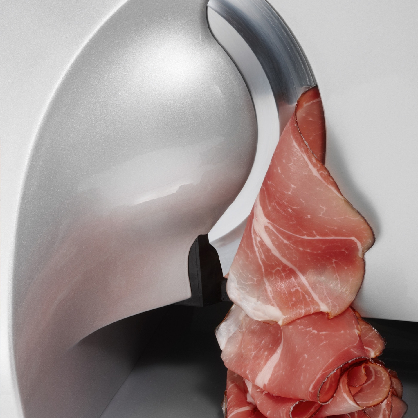 Primo piano di un'affettatrice che taglia sottili fette di prosciutto.