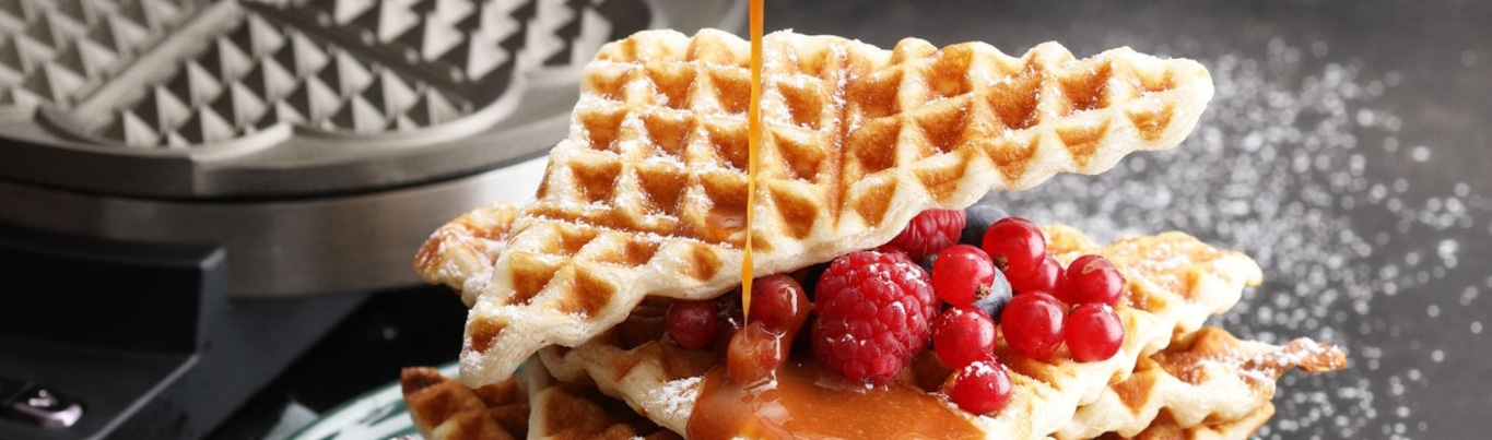 Waffles with berries and syrup being served on a plate, close-up shot