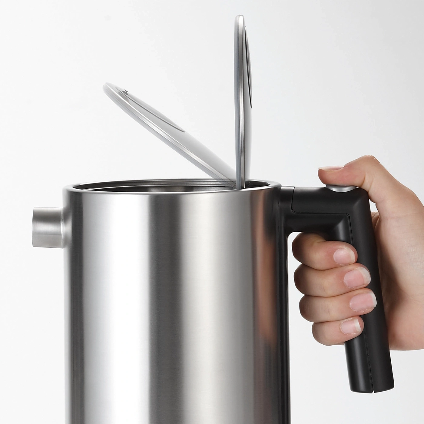 Bouilloire avec couvercle ouvert et poignée, tenue par une main, acier inoxydable