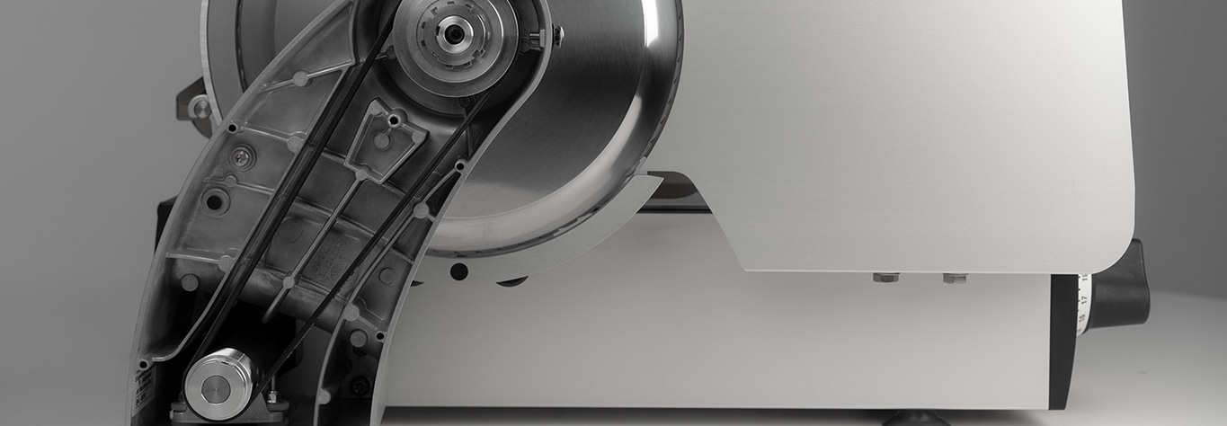 Close-up of a meat slicer with a sharp blade and a black belt, industrial design.