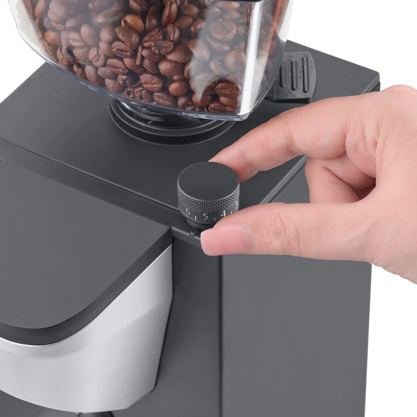 Mano che gira una manopola nera su un macinacaffè con chicchi di caffè