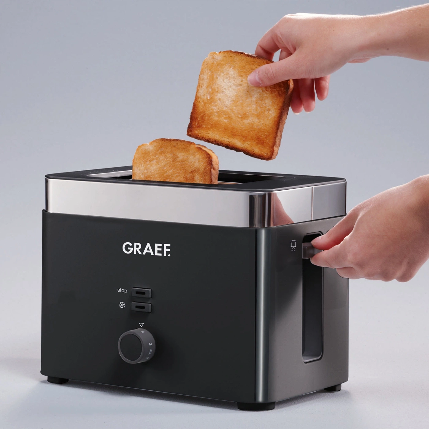 Toaster with toast. Person removing toast. Black toaster with silver accents and GRAEF logo.