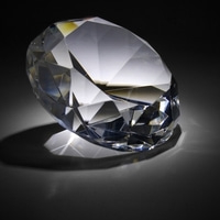 A diamond sparkling on a dark surface, reflecting light and shadows.