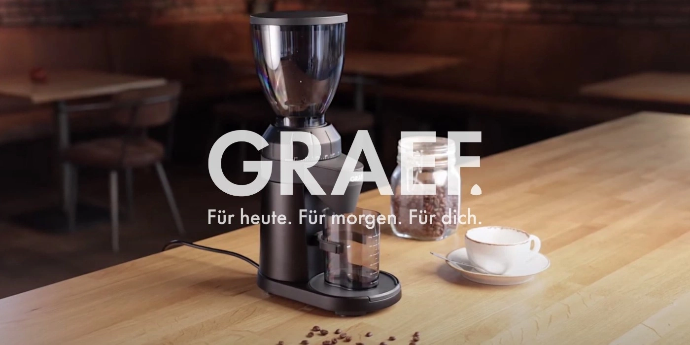Macinacaffè con chicchi di caffè e tazza su un tavolo di legno. GRAEF.