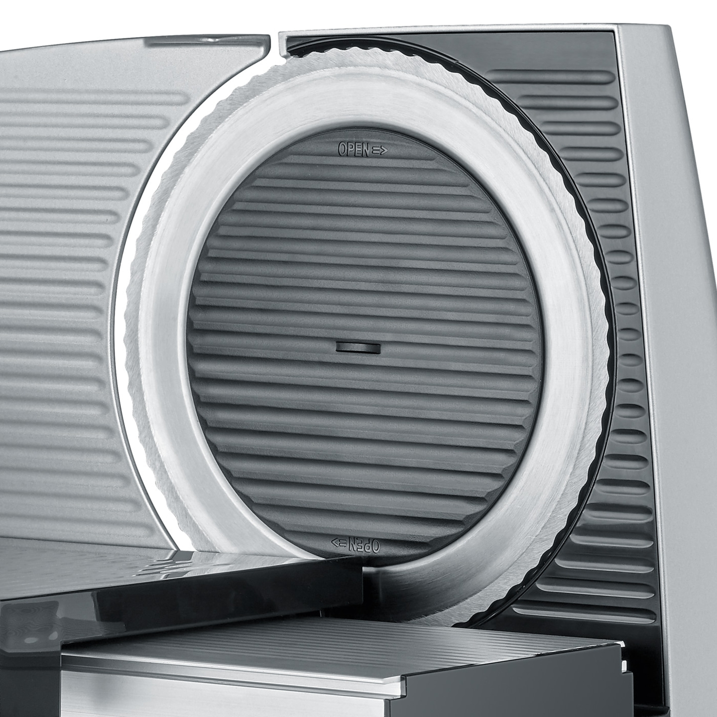Close-up of a silver meat slicer with a circular blade and the word "OPEN" printed on it.