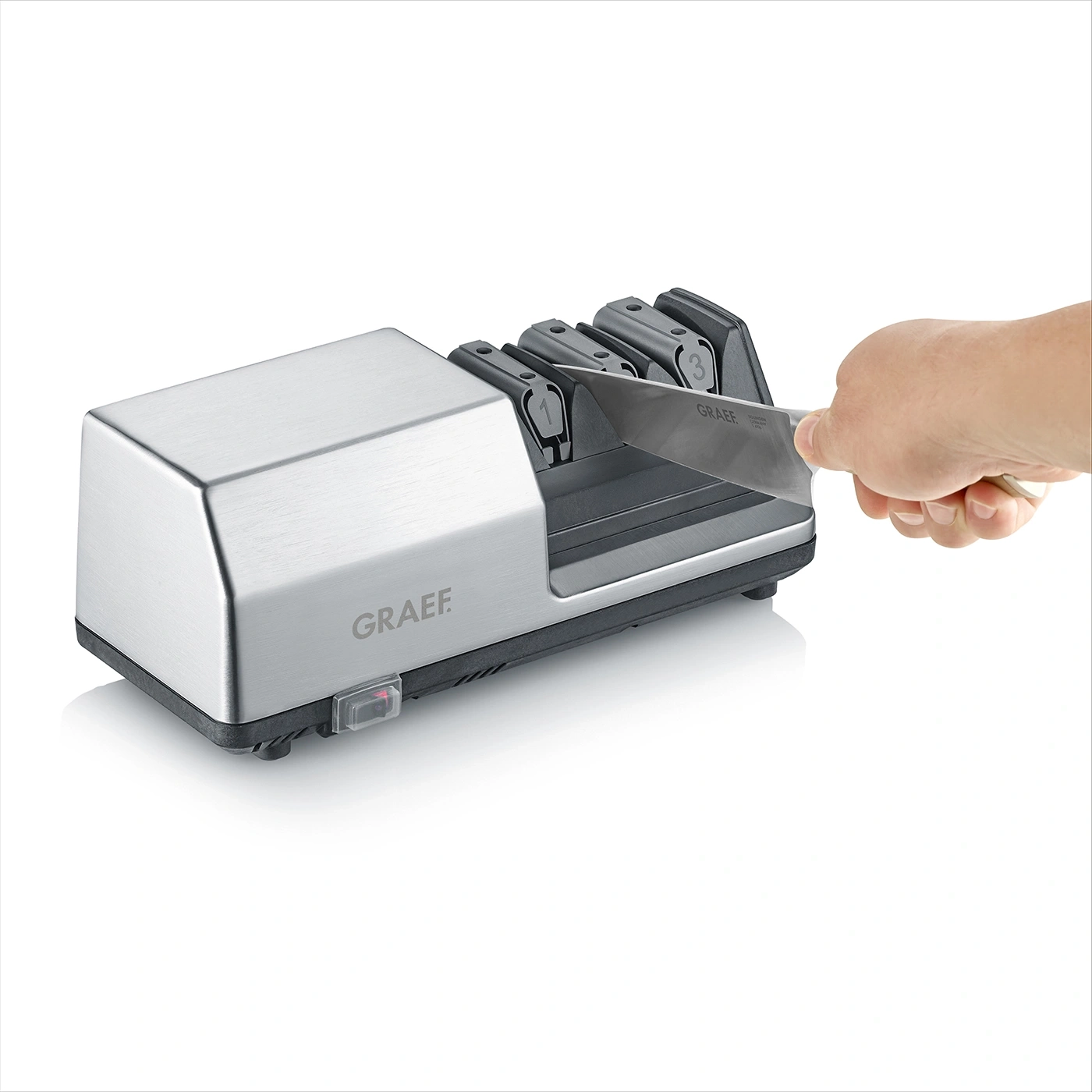 Knife being sharpened with electric sharpener. Hand holding knife. Graef logo visible.
