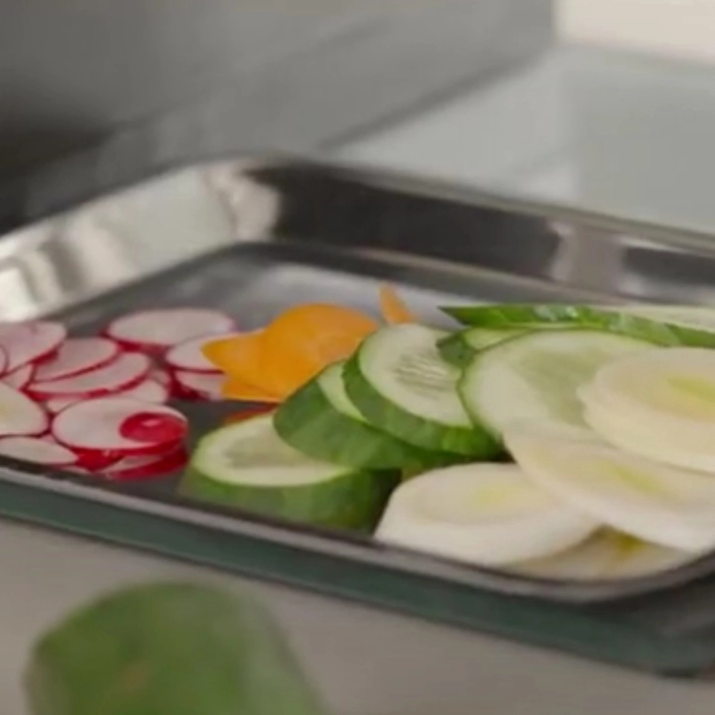 Sliced vegetables: radishes, cucumbers, and carrots on a tray, close-up shot