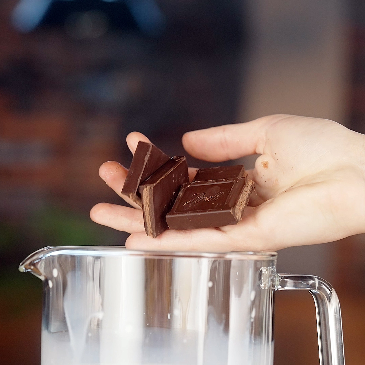 Main tenant des morceaux de chocolat au-dessus d'un verre de lait.