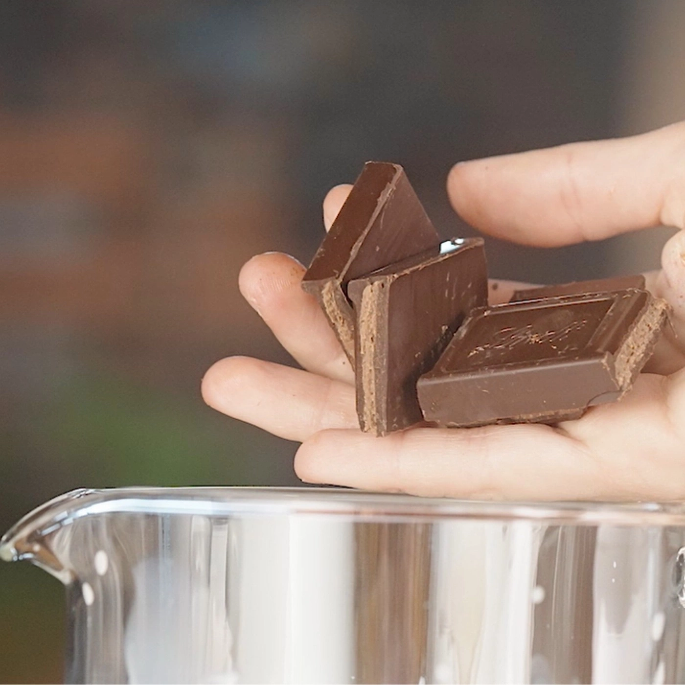 Mains tenant des morceaux de chocolat au-dessus d'un récipient en verre, gros plan.
