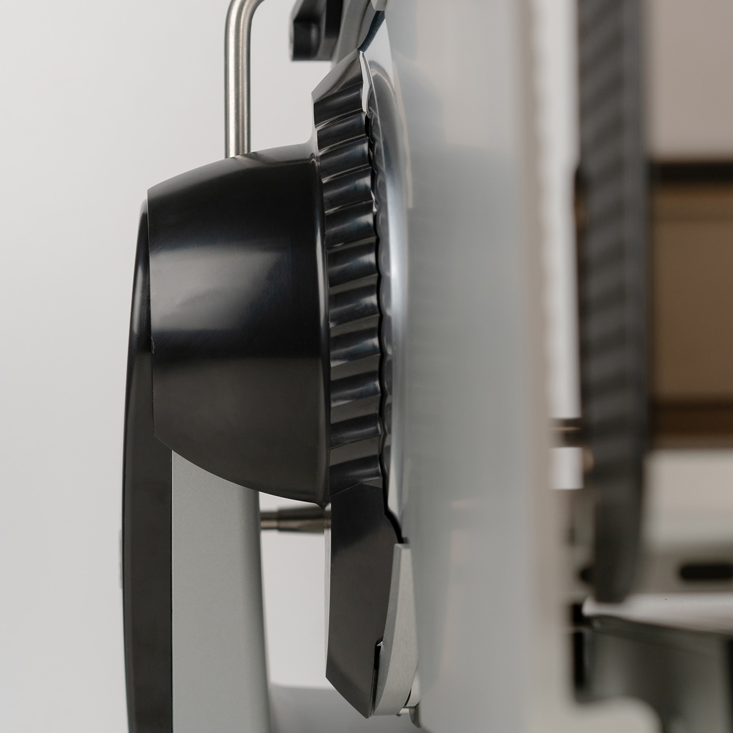 Close-up of a black kitchen machine with a serrated wheel and metal bar