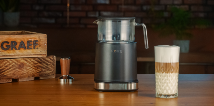 Macchina da caffè con contenitore in vetro e latte macchiato su un tavolo di legno