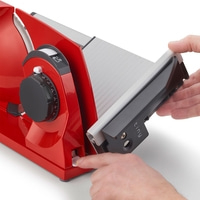 Red meat slicer being operated by two hands, with close-up details.