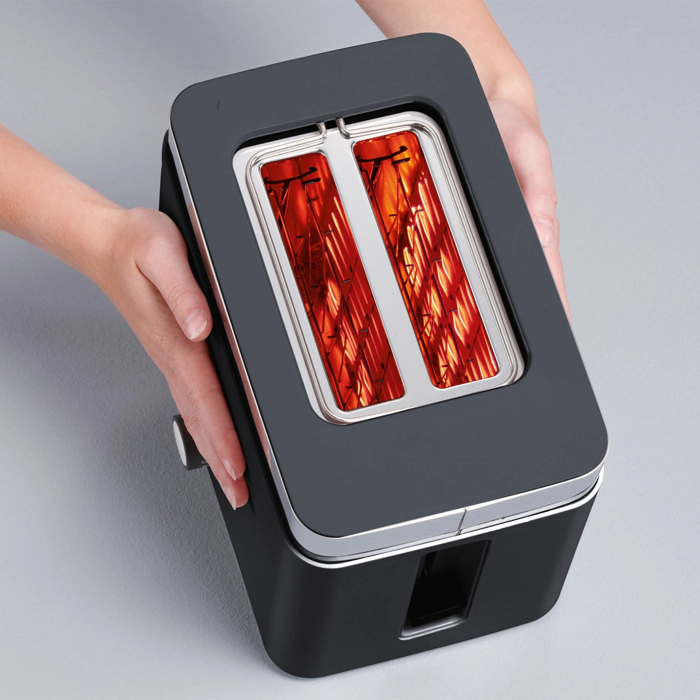 Black toaster held by hands, silver accents, glowing red toast slots, modern design.